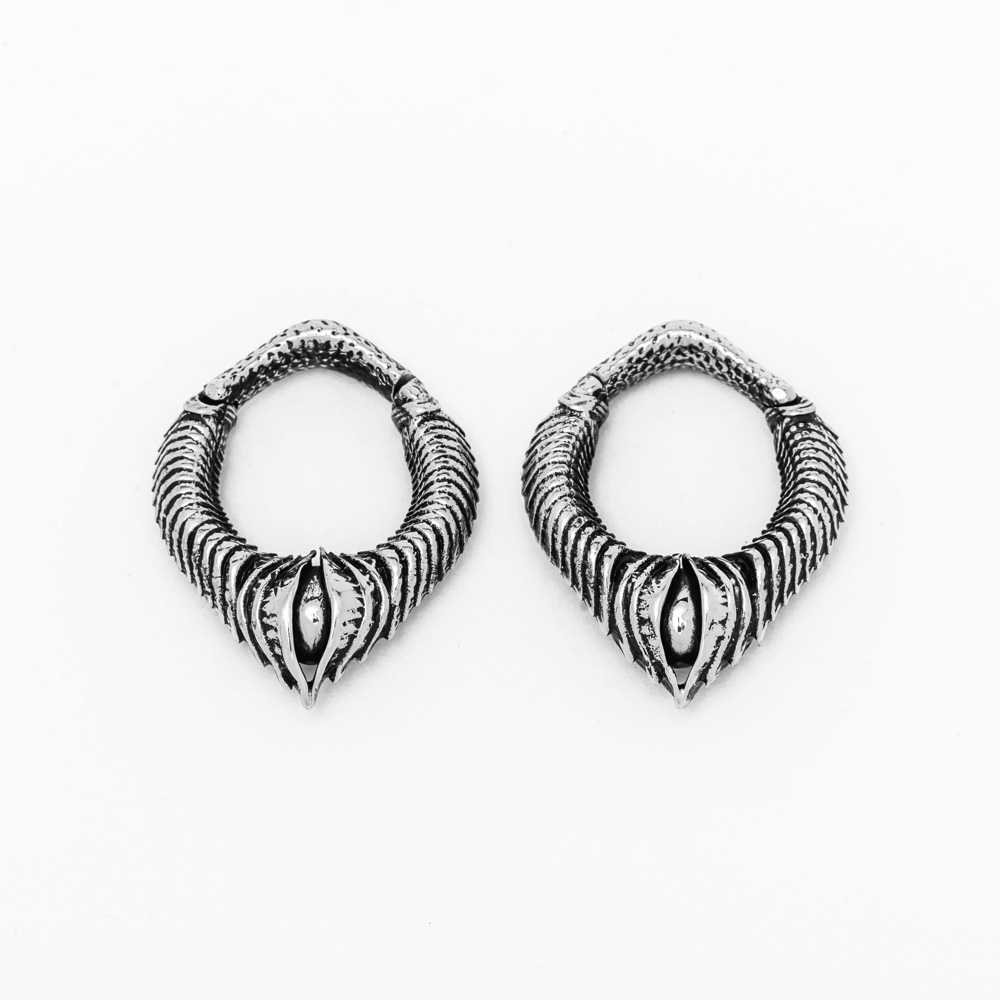 The MARVDASHT Small Biomechanical Clicker Ear Weights in 925 Silver by Kaya Movement, showcased against a white background, feature intricately designed hoops with a textured ribbed pattern tapering to a pointed tip. Their unisex gauge design and central marquise-shaped detail exude sci-fi vibes, enhancing their ornate appearance.